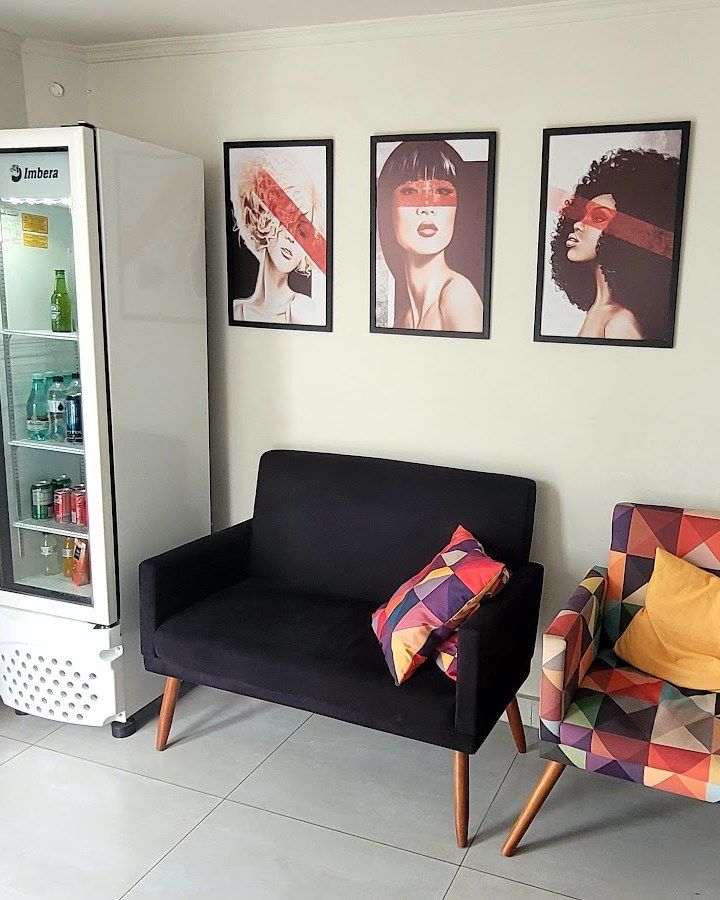 Frigobar com bebidas, sofá e poltrona colorida com quadros na parede